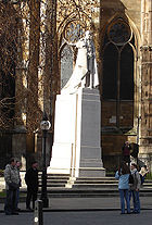 Blanca estatua de piedra de George V en túnicas de liga en un pedestal de la misma piedra de pie en una calle